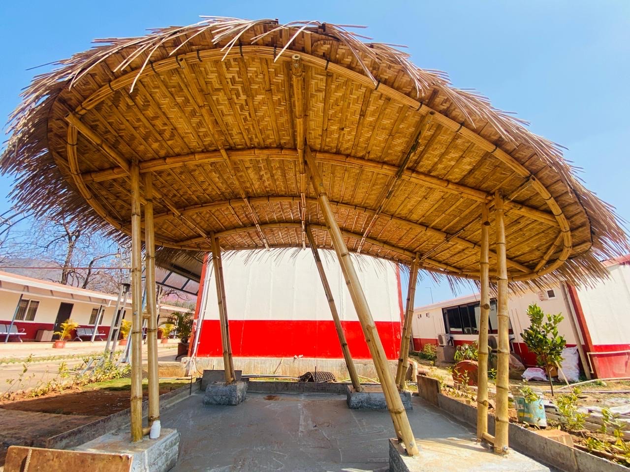 Curved bamboo pavilion with woven canopy on structural bamboo poles in a garden setting, Guwahati